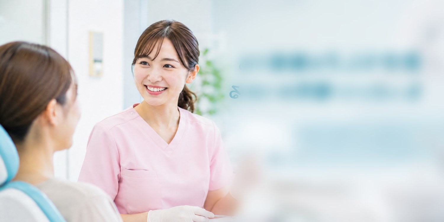 ピンクの制服を着た笑顔の歯科衛生士が患者と話している様子(自分らしさを職場でも/もっといい場所みつかる)